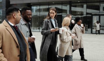 Group of smart people with coats walking and drinking take away coffee