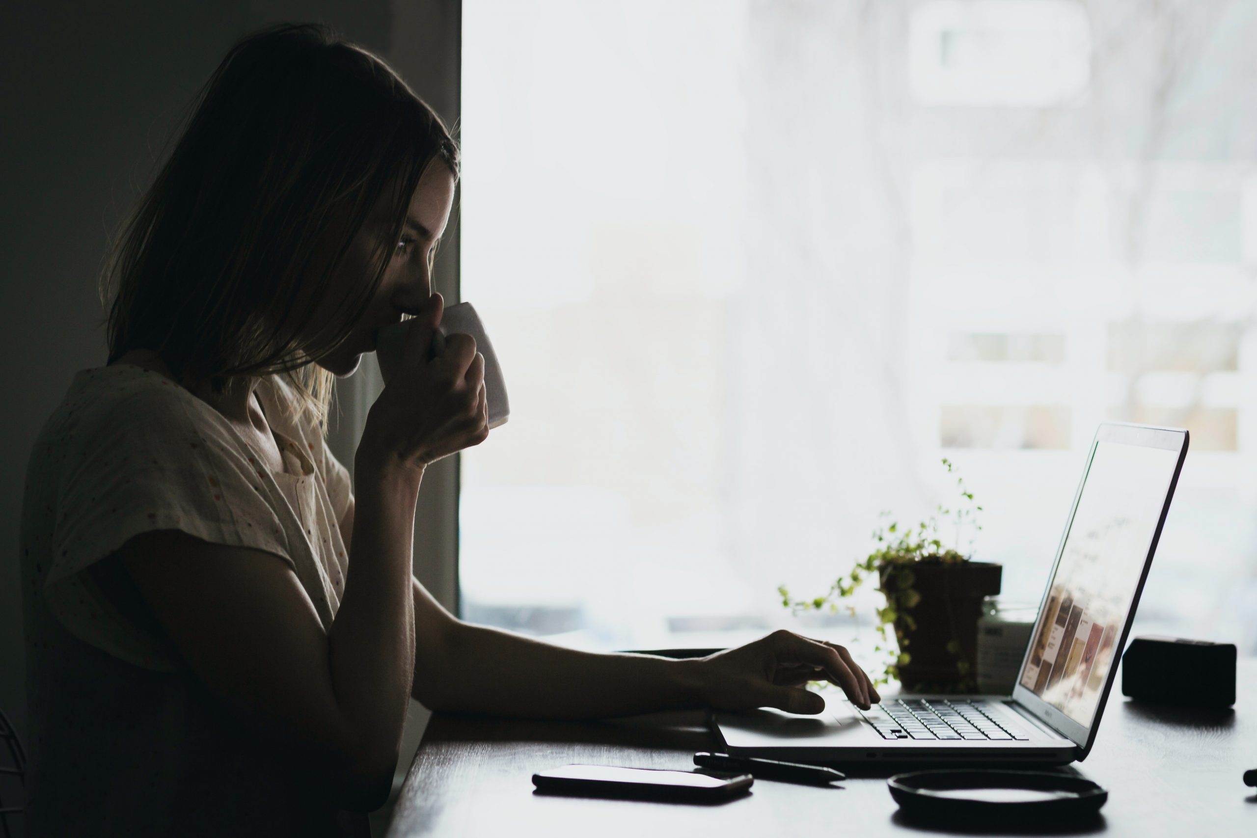 Woman drinking coffee at work at a loptop
