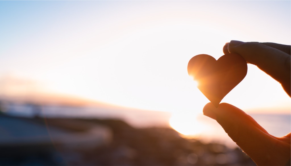 Hand holding heart rock at sunset